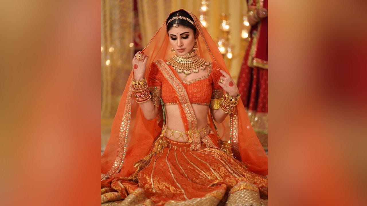 ફોટામાં મૌની રોય ઓરેન્જ એન્ડ ગોલ્ડન ડિટેલ્સવાળા લહેંગા-બ્લાઉઝ સેટમાં ખૂબ જ સુંદર દેખાઈ રહી છે. (Image: Instagram)