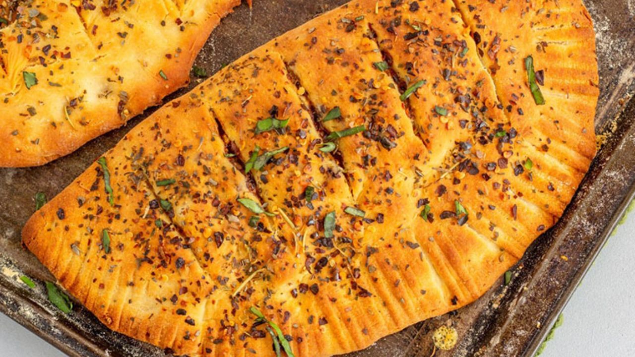 હવે બ્રેડની સ્લાઈસ લો અને તેના પર બ્રશની મદદથી સારી રીતે ગાર્લિક બટર લગાવી દો. હવે તેના પર કોર્ન, ટમાટર સહિતની વસ્તુની ટોપિંગ કરો. ત્યારબાદ તેના પર મોઝેરેલા ચીઝ સારી રીતે પાથરી દો. હવે  ગાર્લિંક બ્રેડનો સ્વાદ વધારવા ઓરેગાનો અને ચિલી ફ્લેક્સ છાંટો.