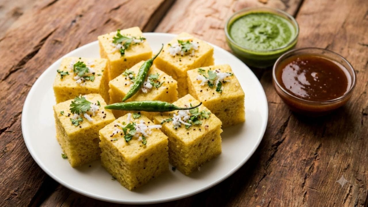 એક નાના પેનમાં તેલ ગરમ કરો. તેમાં રાઈના દાણા ઉમેરો. હવે જ્યારે રાઈના દાણા તતડવા લાગે, ત્યારે તેમાં કઢી પત્તા અને લીલા મરચાં ઉમેરો. ત્યારબાદ થોડી સેકન્ડ માટે હળવા હાથે હલાવો. તેમાં એક કપ પાણી, ખાંડ અને લીંબુનો રસ ઉમેરો અને ઉકળવા દો. ખાંડ ઓગળી જાય પછી ગેસ બંધ કરો. ઠંડા થઈ ગયેલા ઢોકળાને છરી વડે ચોરસ ટુકડામાં કાપી લો. હવે આ તૈયાર કરેલા ખાટા-મીઠા ગરમ વઘારને ચમચી વડે આખા ઢોકળા પર સારી રીતે રેડો, જેથી ઢોકળા બધું પાણી શોષી લે અને એકદમ સરસ બની જાય.