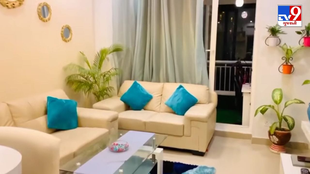 જેઠાલાલના આલીશાન લિવિંગ રૂમમાં ક્રીમ કલરના સોફા વિથ બ્લુ કુશન અને દીવાલ પર ગોલ્ડન મિરર ફ્રેમ્સ દેખાય છે. રૂમની ખૂણામાં રાખેલા છોડ અને દીવાલ પરના વોલ માઉન્ટેડ પ્લાન્ટ્સ આ ઇન્ટિરિયરને નેચરલ અને રોયલ લુક આપે છે. (Image Source | YouTube @Maakasam_Dilip_Joshi)